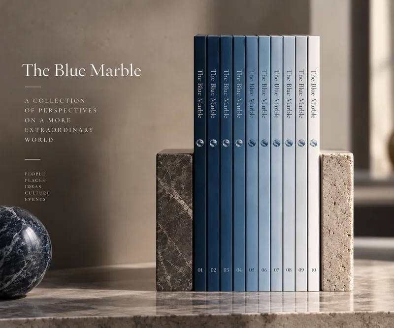 Colección The Blue Marble: diez ediciones numeradas de lomos en degradado de azules, sujetas entre dos sujetalibros de piedra junto a una canica de mármol azul.